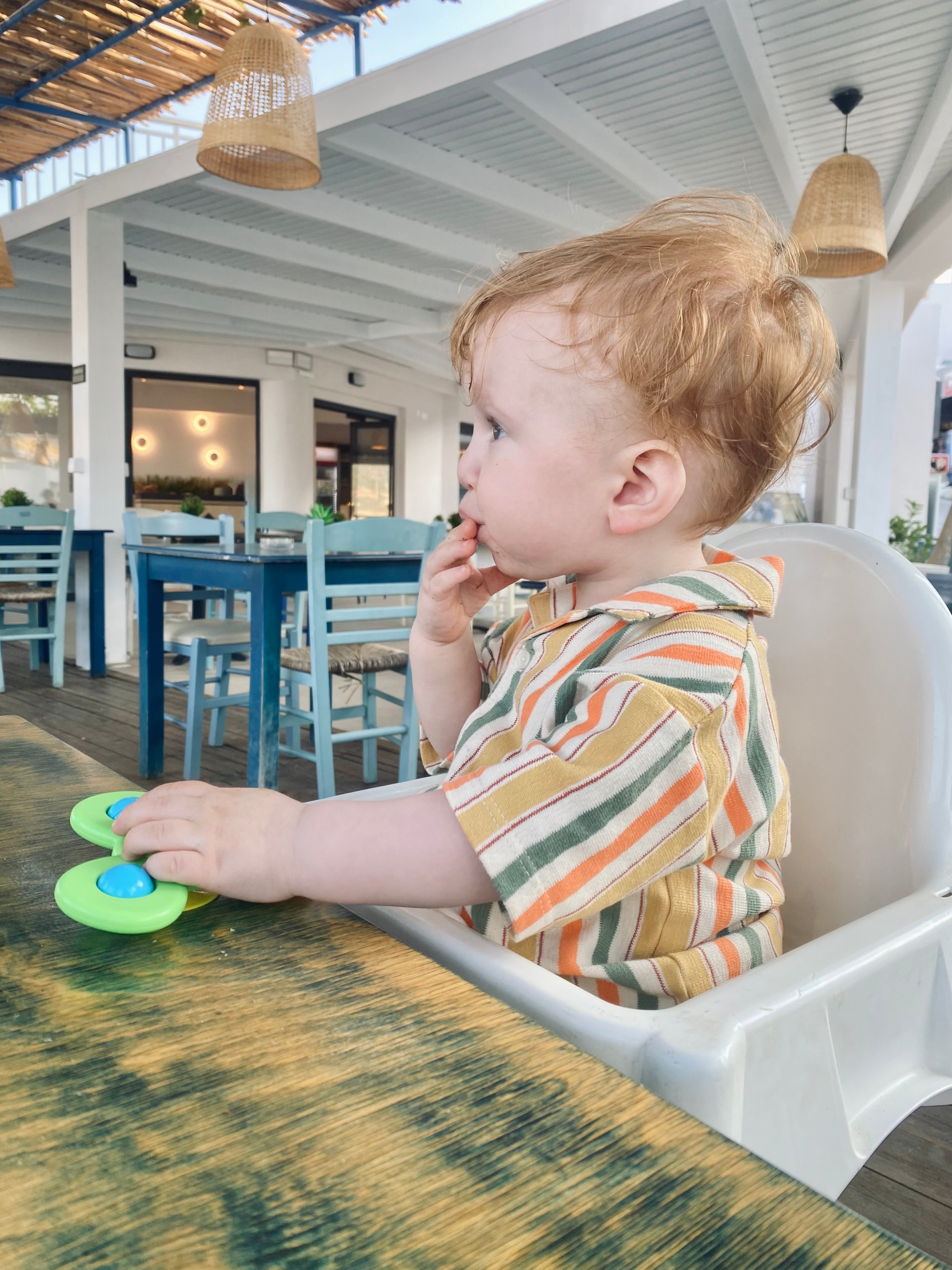 bebis sitter i barnstol på restaurang utomlands på semester i Grekland med en grön Fidget Spinner framför sig och snurar på den i väntan på mat