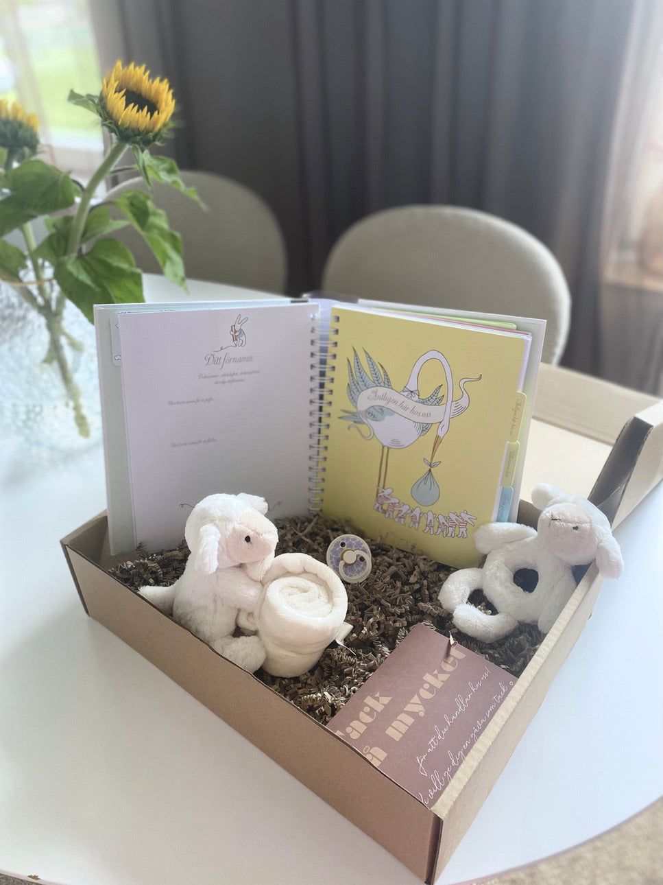 babybok mitt första år som är uppslagen så att man ser en gul soda med en stor stork på. i en presentlåda med en snutteilt, napp och mjuk skallra samt ett tackkort