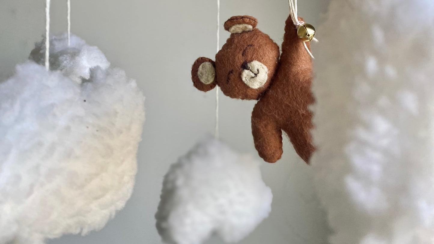 Med motiv av en brun nalle som flyger med röda ballonger bland vita fluffiga moln blir denna mobil både en söt detalj och en mjuk, naturlig accessoar till din spjälsäng i ditt sovrum