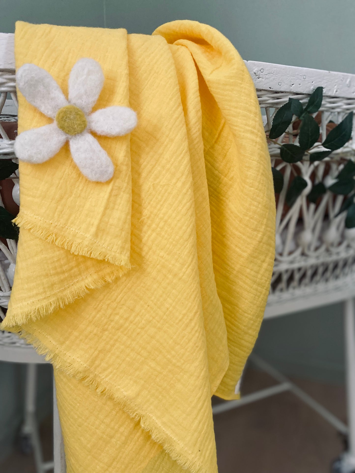 Handgjord gul filt med vit blomma ligger över en vit krubba