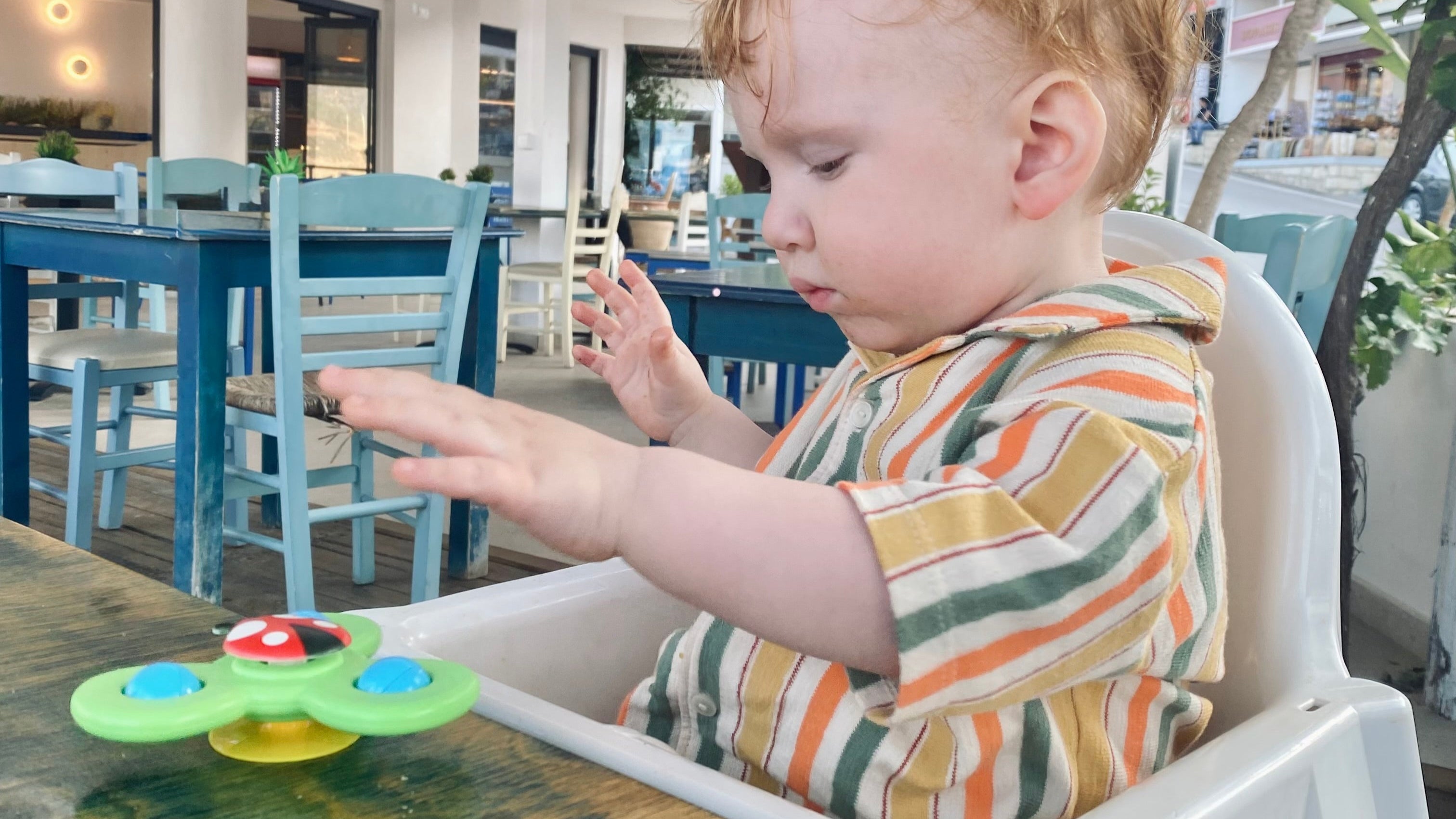 1 årig bebis sitter på restaurang och leker med fidget spinner i väntan på maten