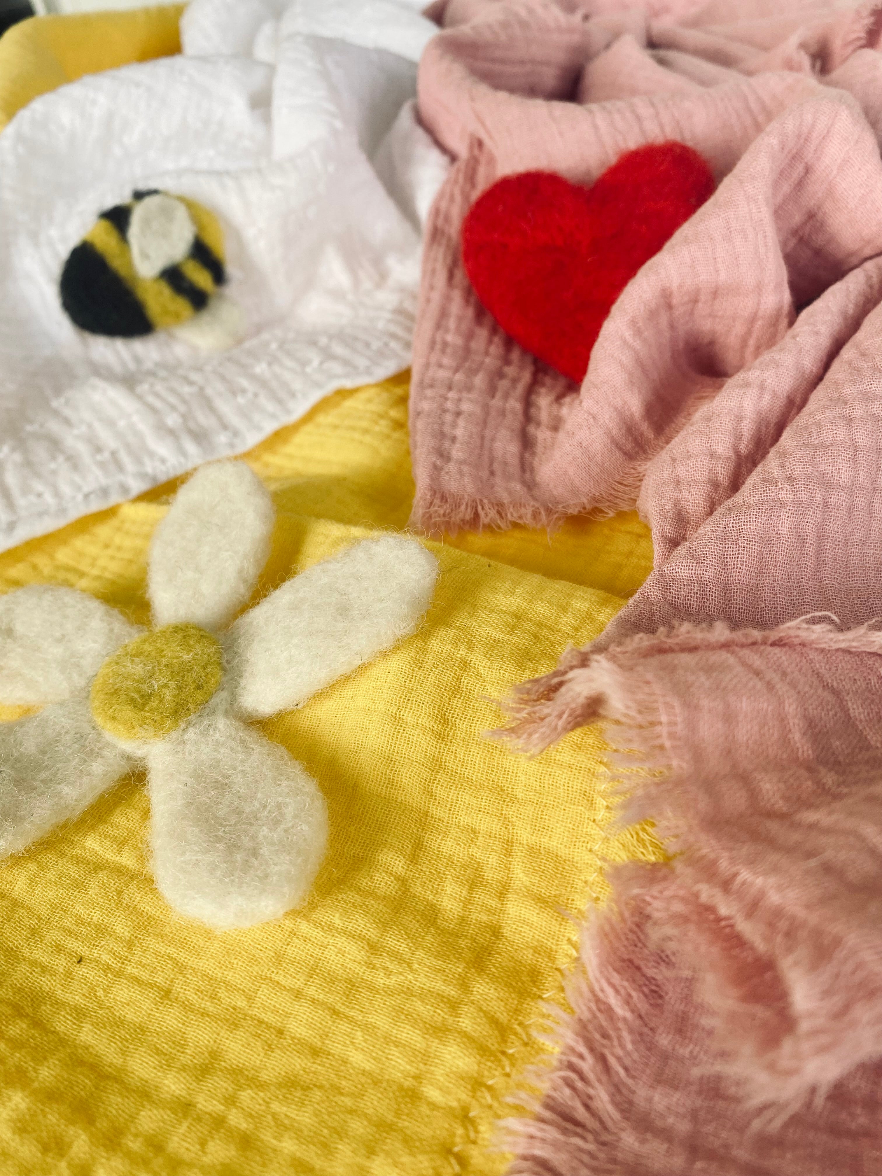 Tre lätta och luftiga filtar i muslin för barn eller baby. En rosa med ett rött hjärta, en gul med en blomma och en vit med en humla