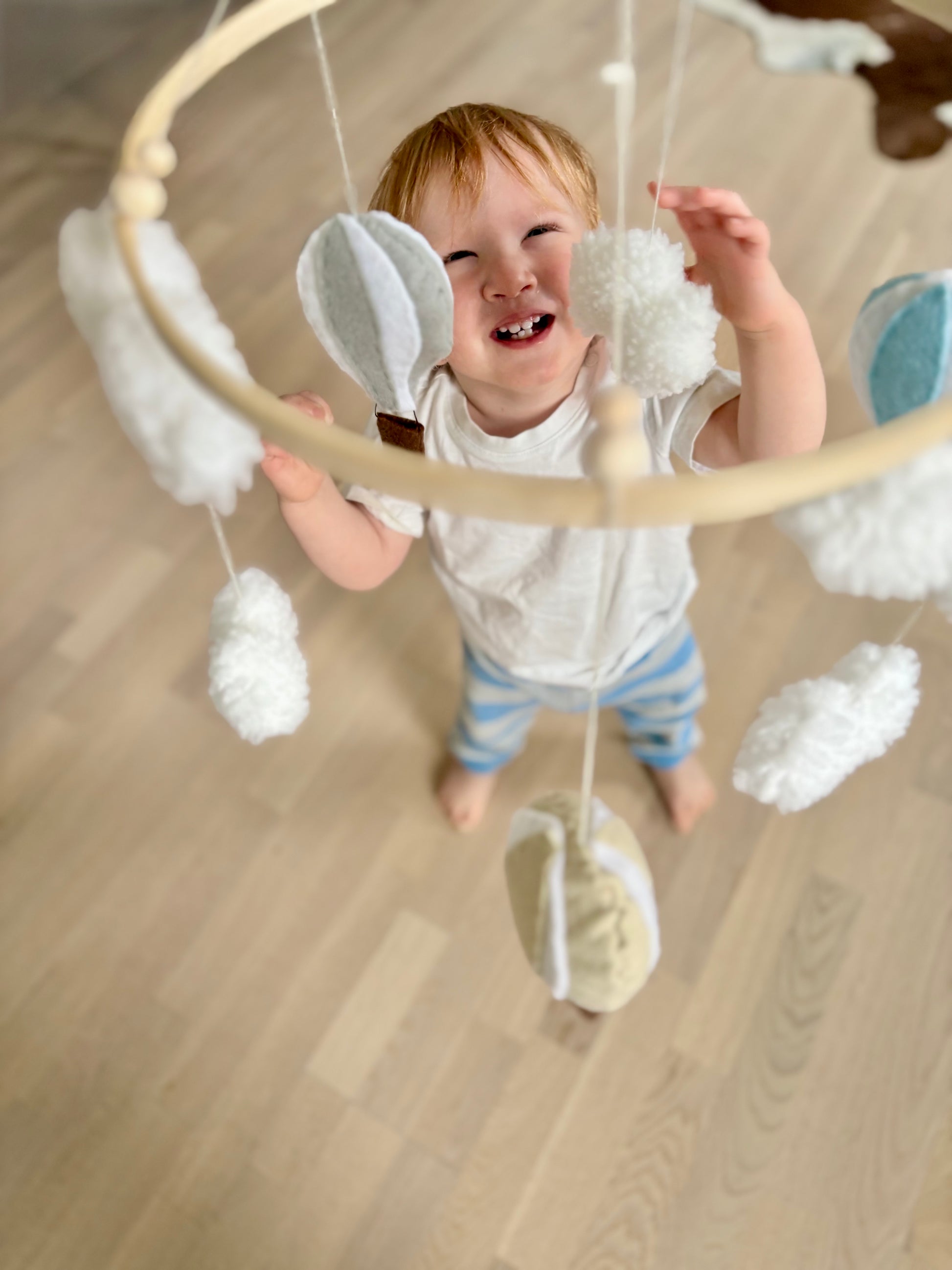Handgjord babymobil med filtballonger och moln hänger över ett litet barn som försöker greppa den