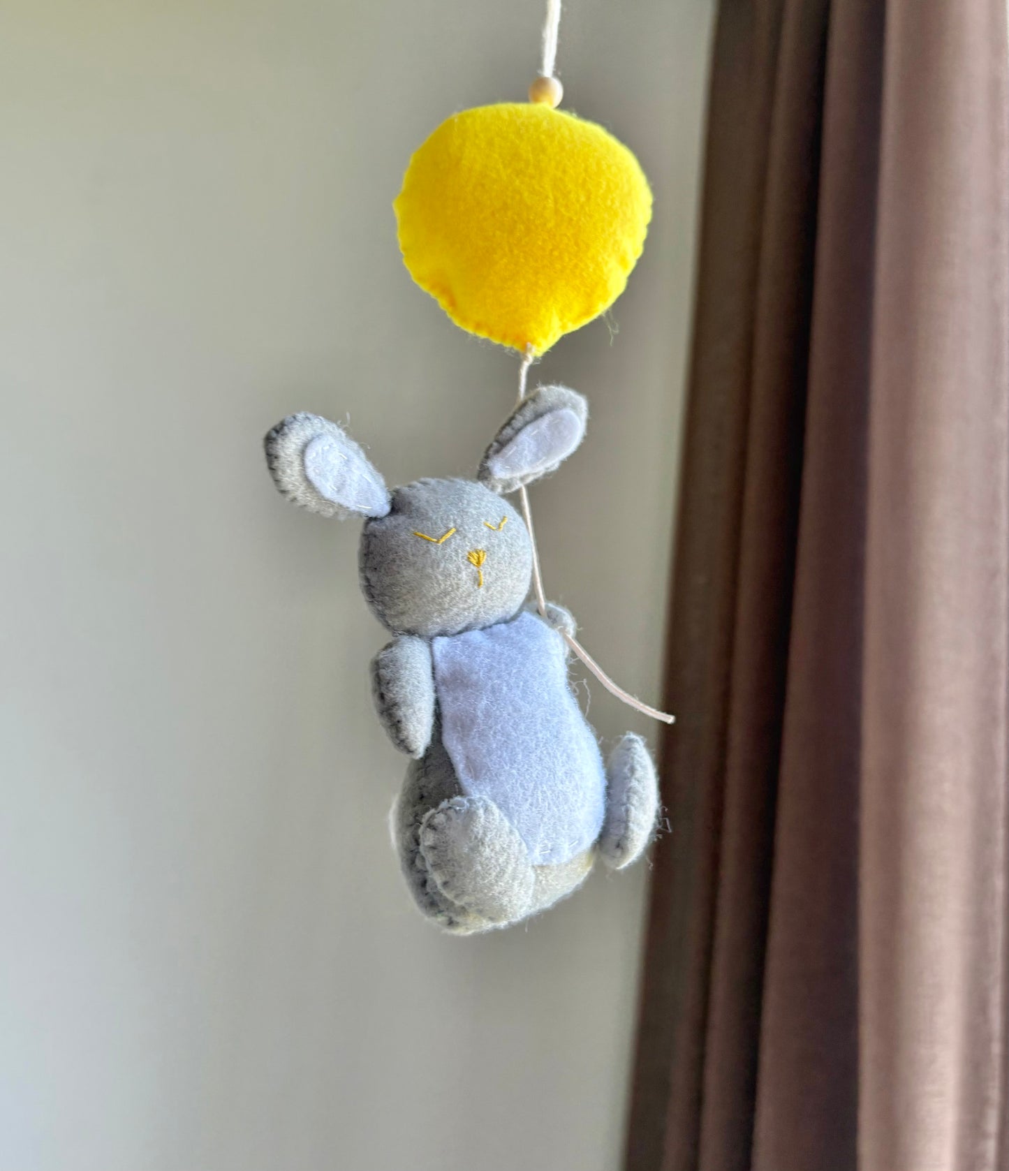 Handgjort barnvagnshänge i filt – grå kanin som håller i gul ballong