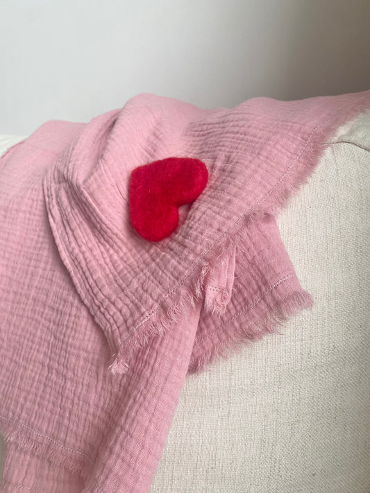 Rosa muslinfilt med rött hjärta ligger på en vit soffa med vit bakgrund