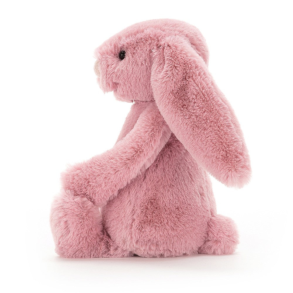 Ett litet rosa mjukisdjur som sitter från sidan i form av en kanin med lång öron och stora fötter